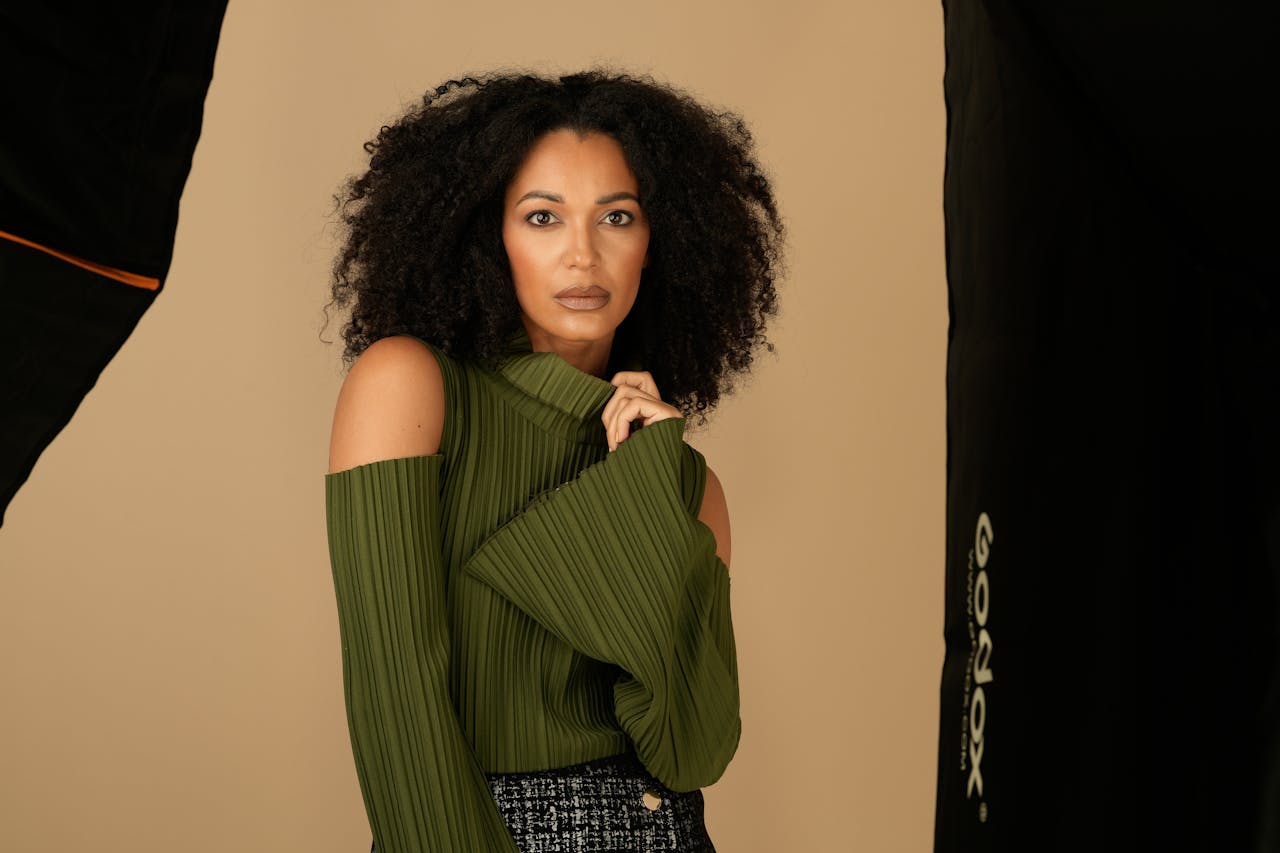 Studio portrait of a woman with curly hair wearing a trendy green sweater against a neutral background.